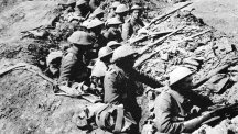 British infantrymen occupy a shallow trench in a ruined landscape before an advance during the Battle of the Somme.