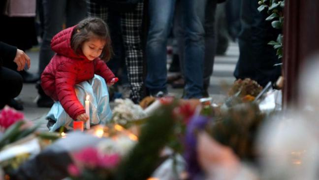 A young girl leaves a lit candle outside Le Carillon bar, Paris, one of the venues for the attacks
