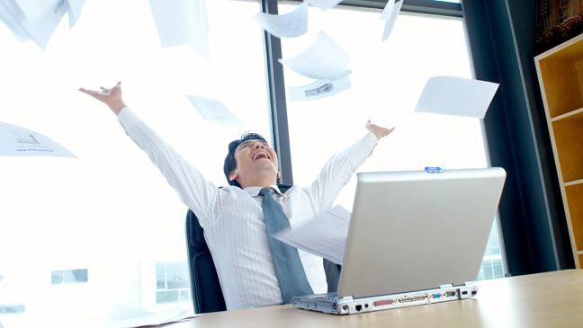 Man throwing papers in the air by laptop